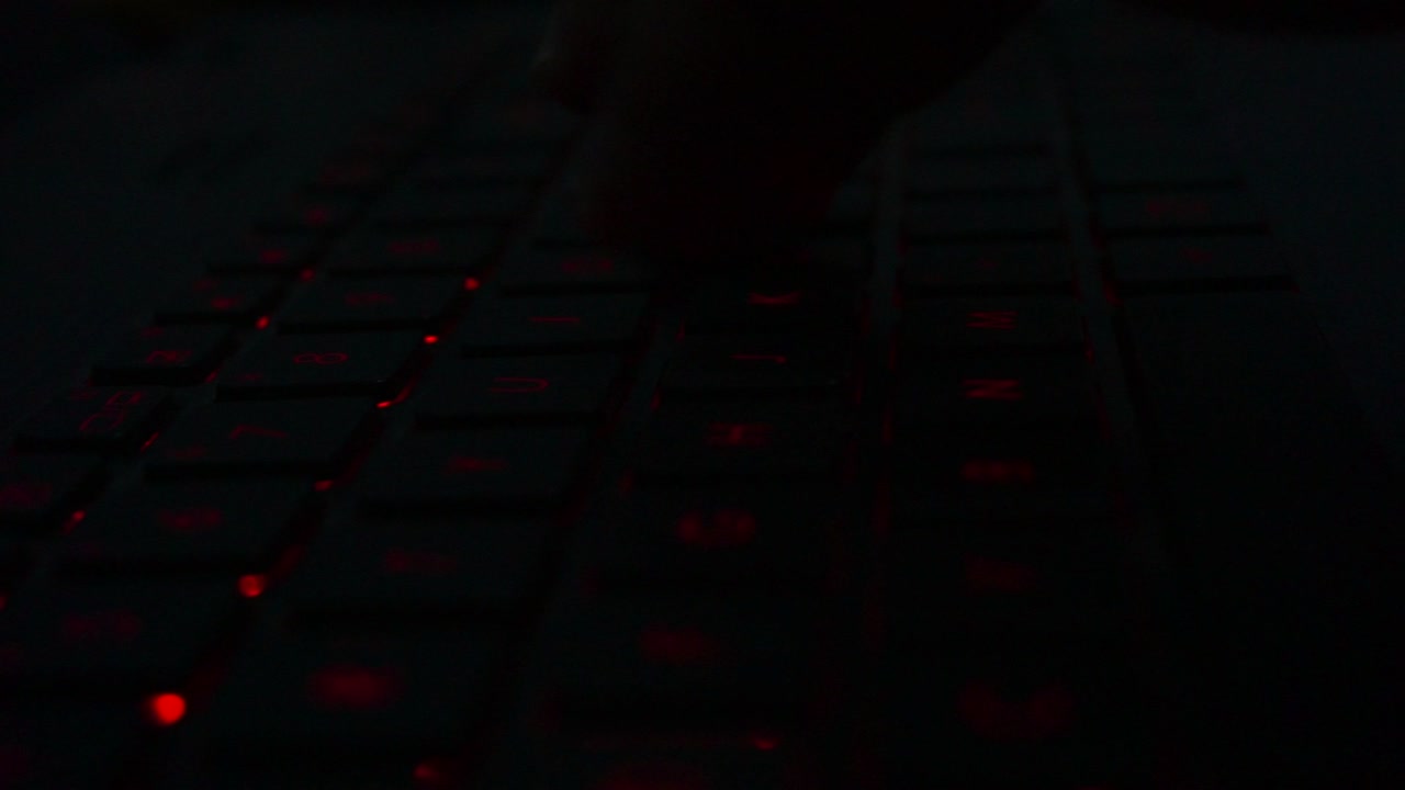 Close up shot of hand typing on red lighting keyboard of laptop in dark room