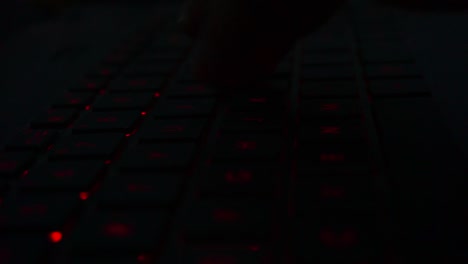 primer plano de la mano escribiendo en el teclado de iluminación roja de la computadora portátil en una habitación oscura