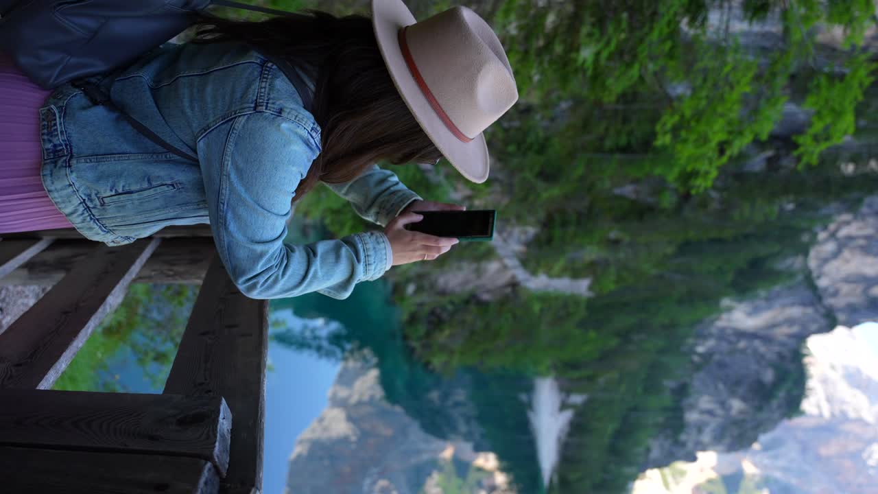 mujer tomando fotografías con un teléfono inteligente en lago di braies, dolomitas, italia