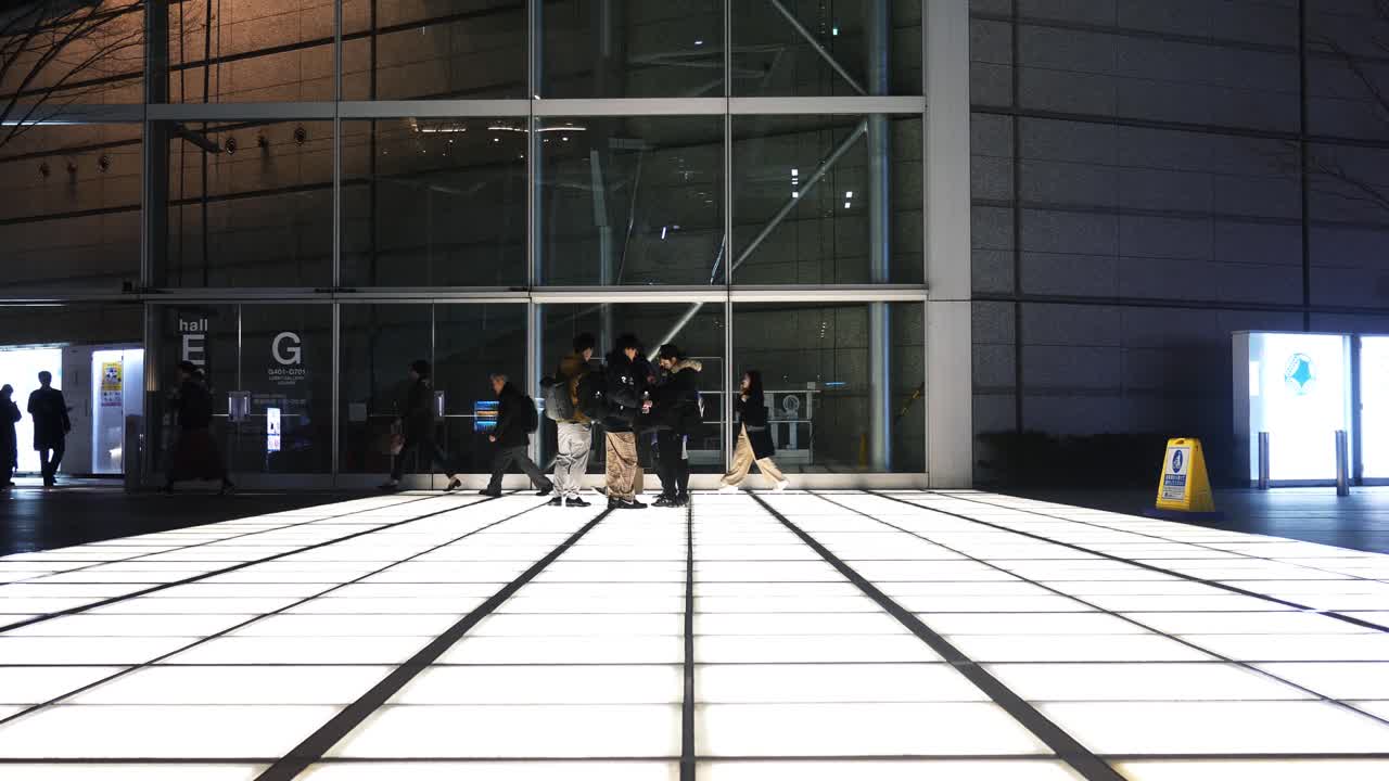 Outside at night Tokyo International Forum light squares with commuters walking past.