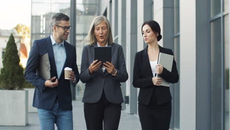 mature businesswoman reading a business project on a tablet and talking with her colleagues while walking in the street