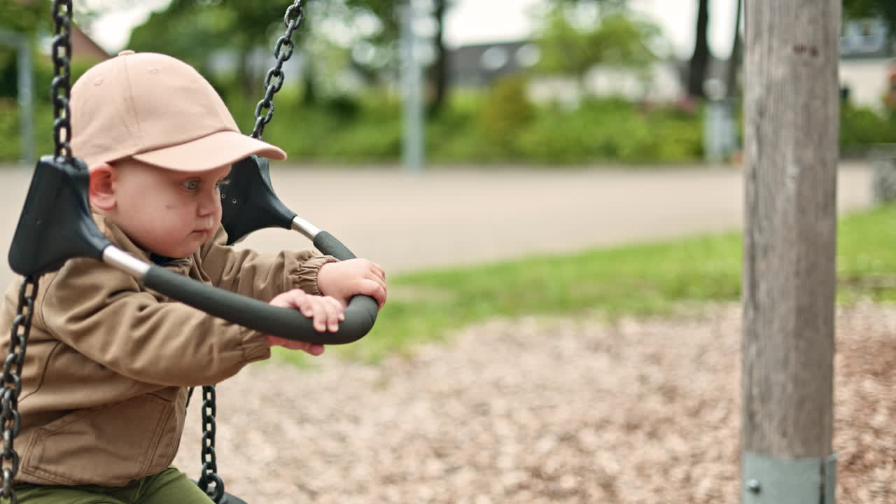 Cute 2 year old boy swinging on a swing on a playground. Child swinging while walking outdoors. Outdoor activities for children