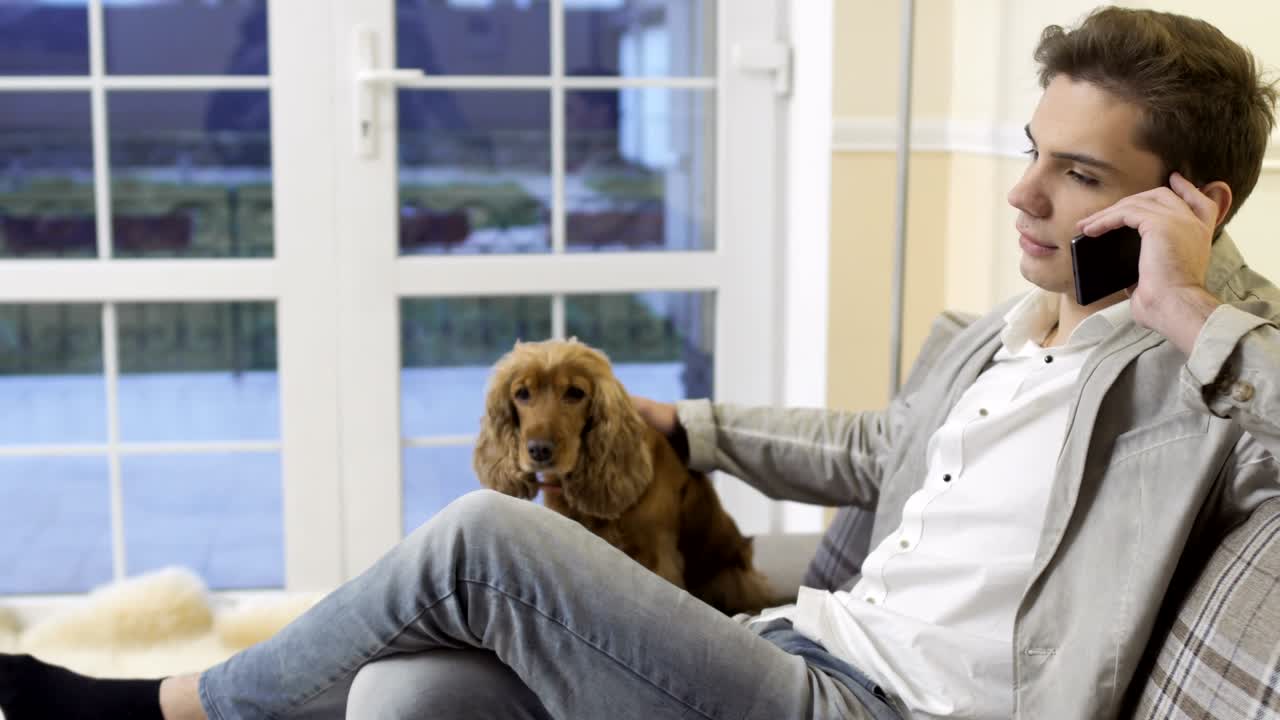 joven se relaja en casa en el sofá hablando por teléfono y acaricia a su perro