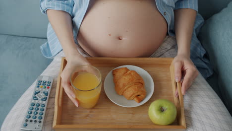 pregnant woman relaxing on sofa with breakfast