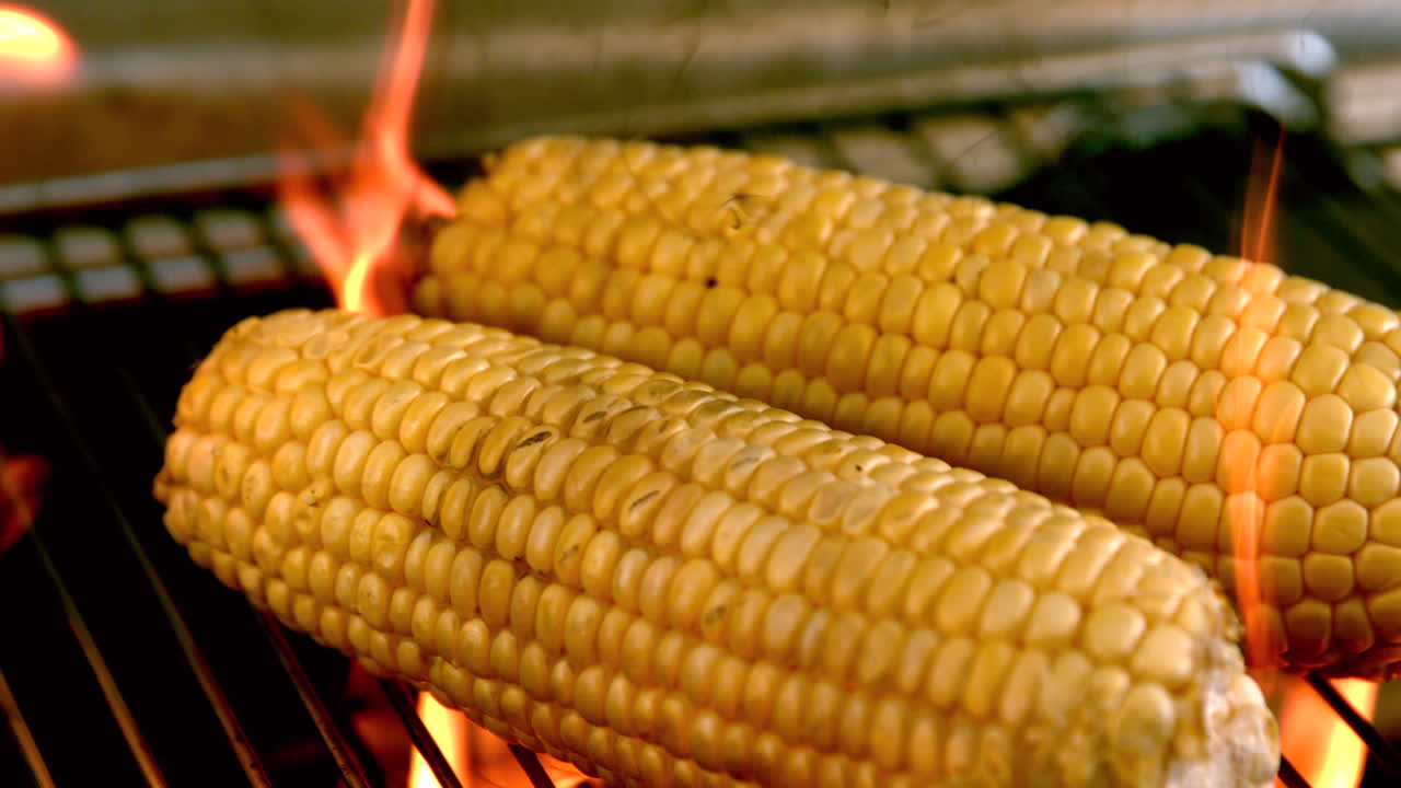 Corn on the cob being cooked on flaming barbecue