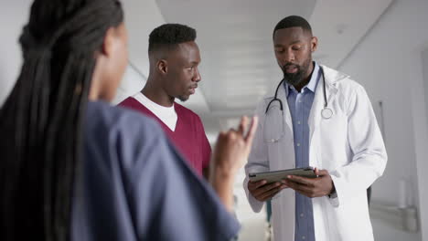 Diverse-male-and-female-doctors-discussing-work,-using-tablet-in-corridor-at-hospital,-slow-motion