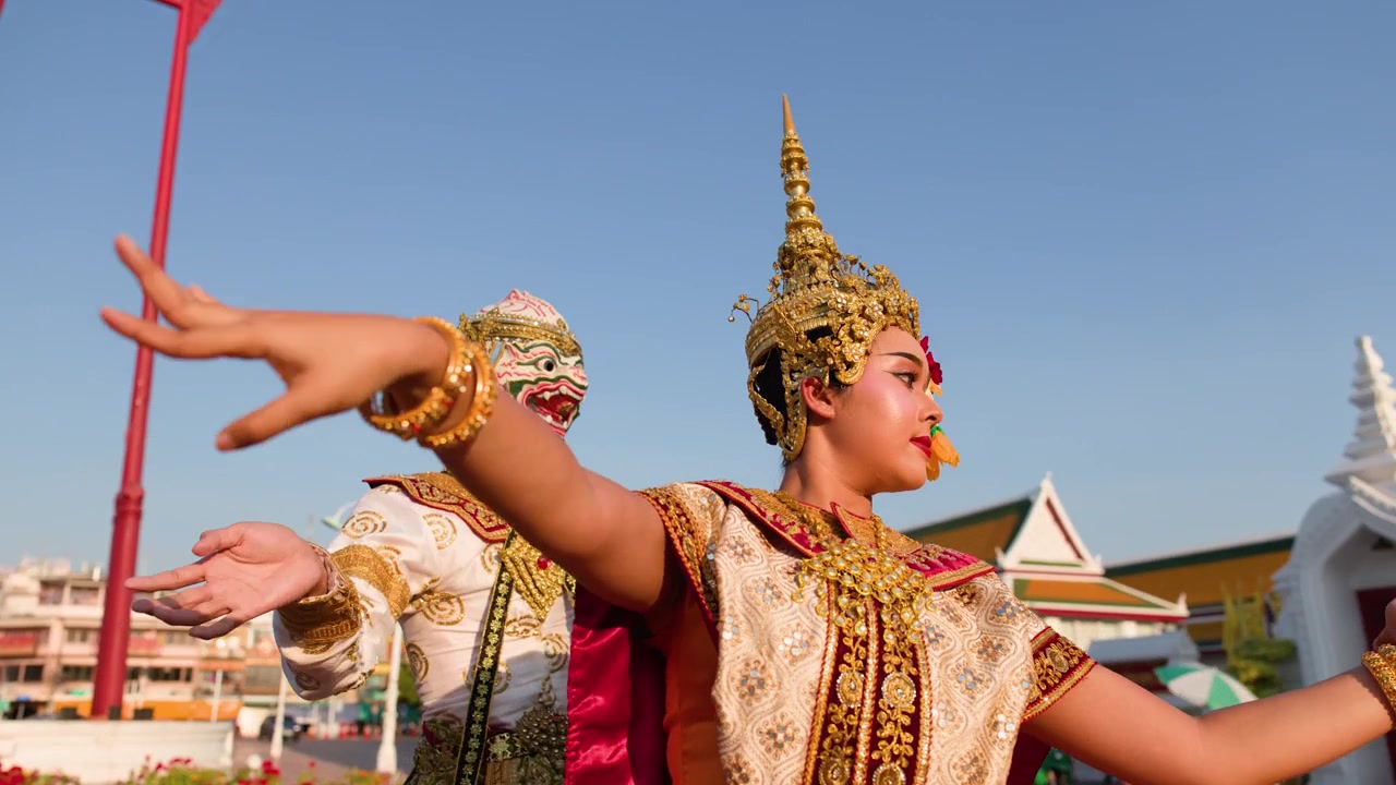 Penari bertopeng dan berkostum menampilkan gerakan tari tradisional Thailand di luar ruangan di bawah langit biru cerah.