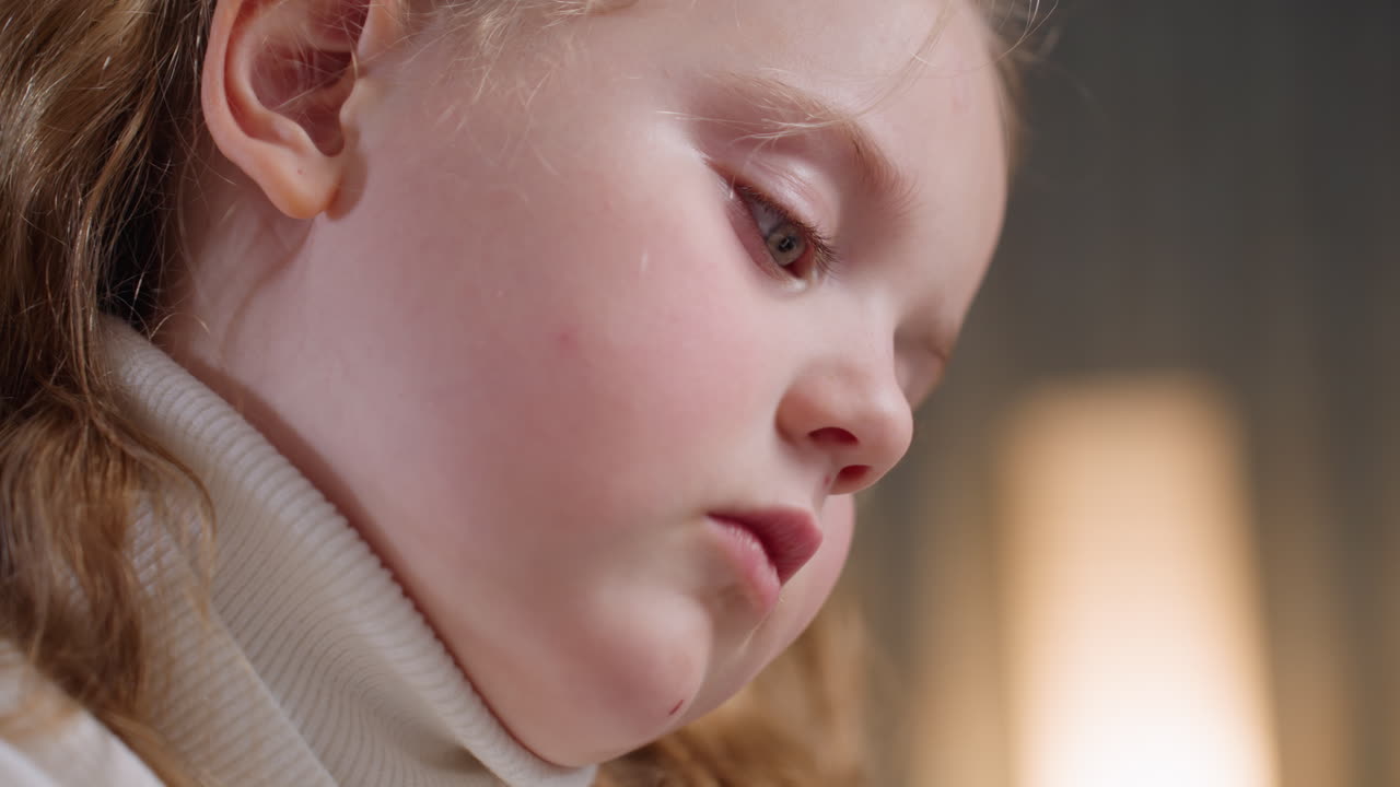 Close up of student with blonde hair wearing white turtleneck sweater showing serious face with deep concentration while studying and focusing on drawing, symbolizing childhood learning, intelligence