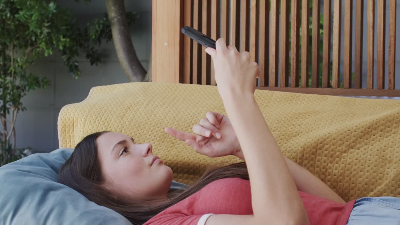 뒤로 누워서 슬로우 모션으로 스마트폰으로 문자 메시지를 보내는 사려 깊은 백인 십대 소녀