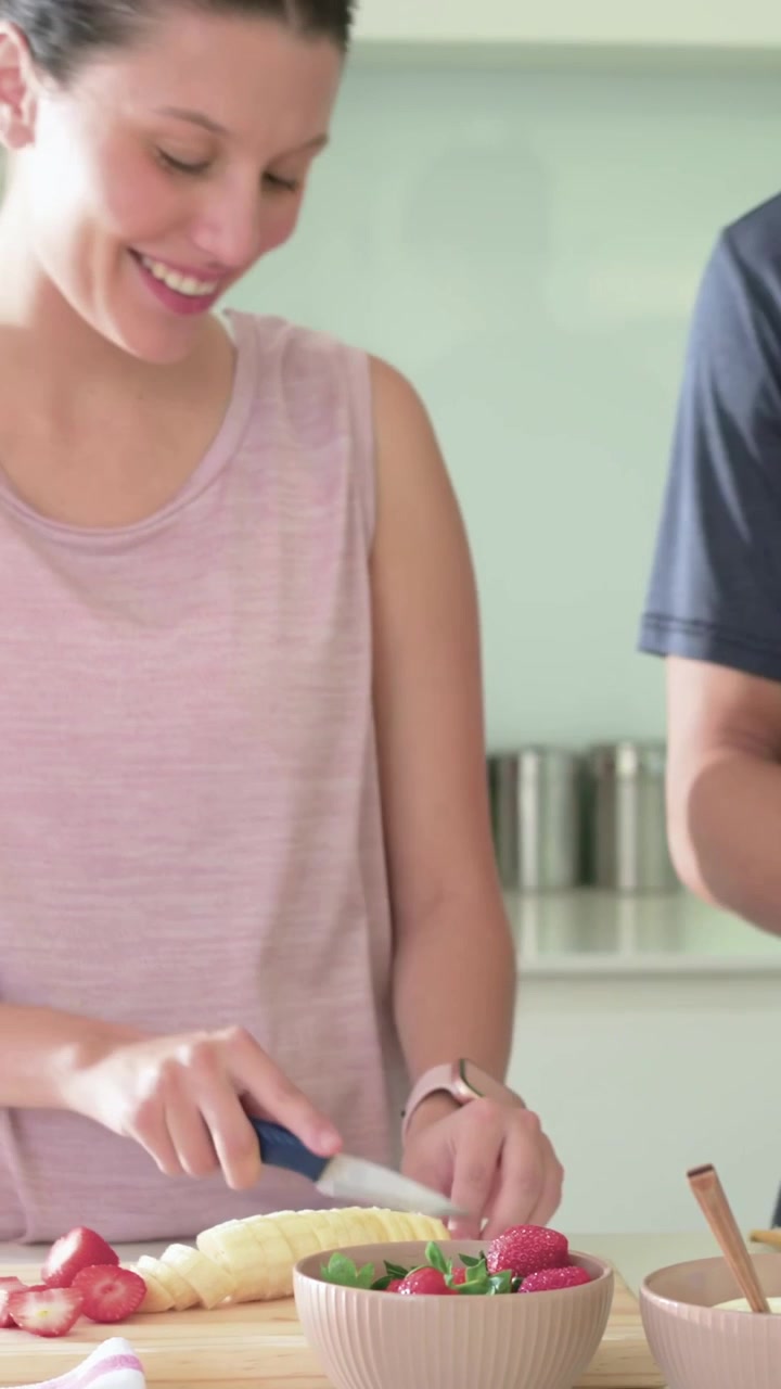Video verticale: Donna che inizia la preparazione in cucina, con top rosa, affetta frutti di bosco e banana per una ciotola