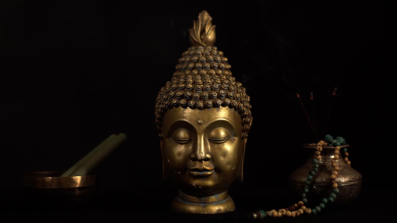 cabeza de bronce del buda con cuenco tibetano y palos de incienso en llamas, fondo oscuro