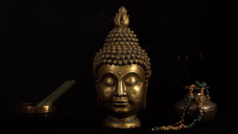 Bronze-head-of-the-Buddha-with-tibetian-bowl-and-burning-incense-sticks,-dark-background