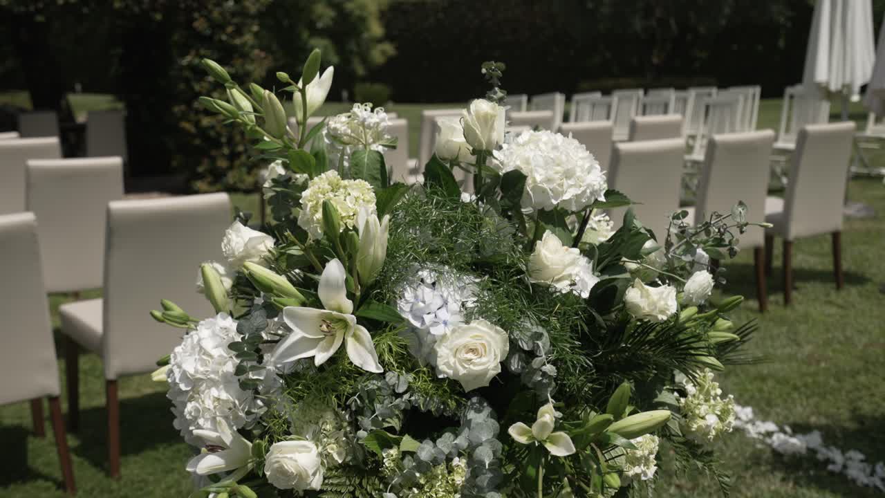 Elegante composizione floreale bianca con rose, gigli e ortensie, allestita per una cerimonia di matrimonio all'aperto.