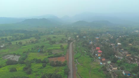 falling drone shot over rural indian road hills background green