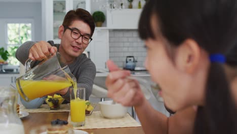 부 ⁇ 에서 행복한 아시아 아버지가 아침 식사를 하고 웃는 아들과 딸을 위해 주스를  ⁇ 고 있습니다.