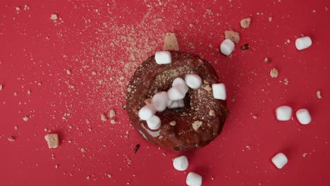 decorating chocolate donut with white marshmallows, red table background, slowmo