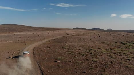 Drone-Siguiendo-La-Conducción-Rápida-Del-Automóvil-En-Polvorientas-Y-Remotas-Tierras-Altas-En-Islandia.-Vehículo-De-Vista-Aérea-Explorando-El-Campo-Islandés-Conduciendo-Revolviendo-La-Nube-De-Polvo.-Concepto-De-Seguro-Y-Libertad