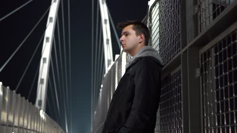 young white male teen standing on a bridge at night looking around