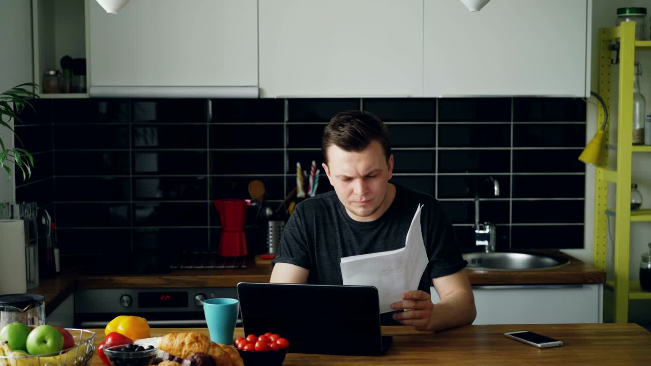 joven preocupado pagando facturas en línea usando una computadora portátil en el kithcen en casa