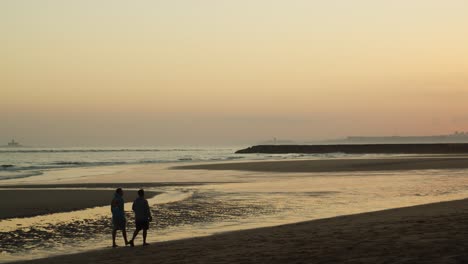 two male friends walking on beach at sunset, handheld wide shot