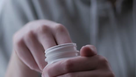 close-up of a woman hands opening a jar of dietary supplements and taking out a capsule