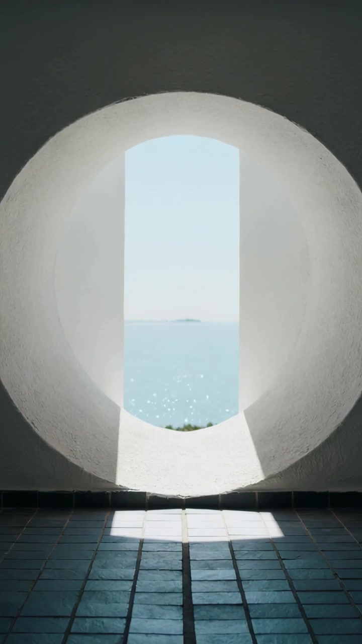 Vídeo vertical: Luz solar em movimento, abertura redonda emoldurando o mar e a ilha, projetando uma mancha nas telhas