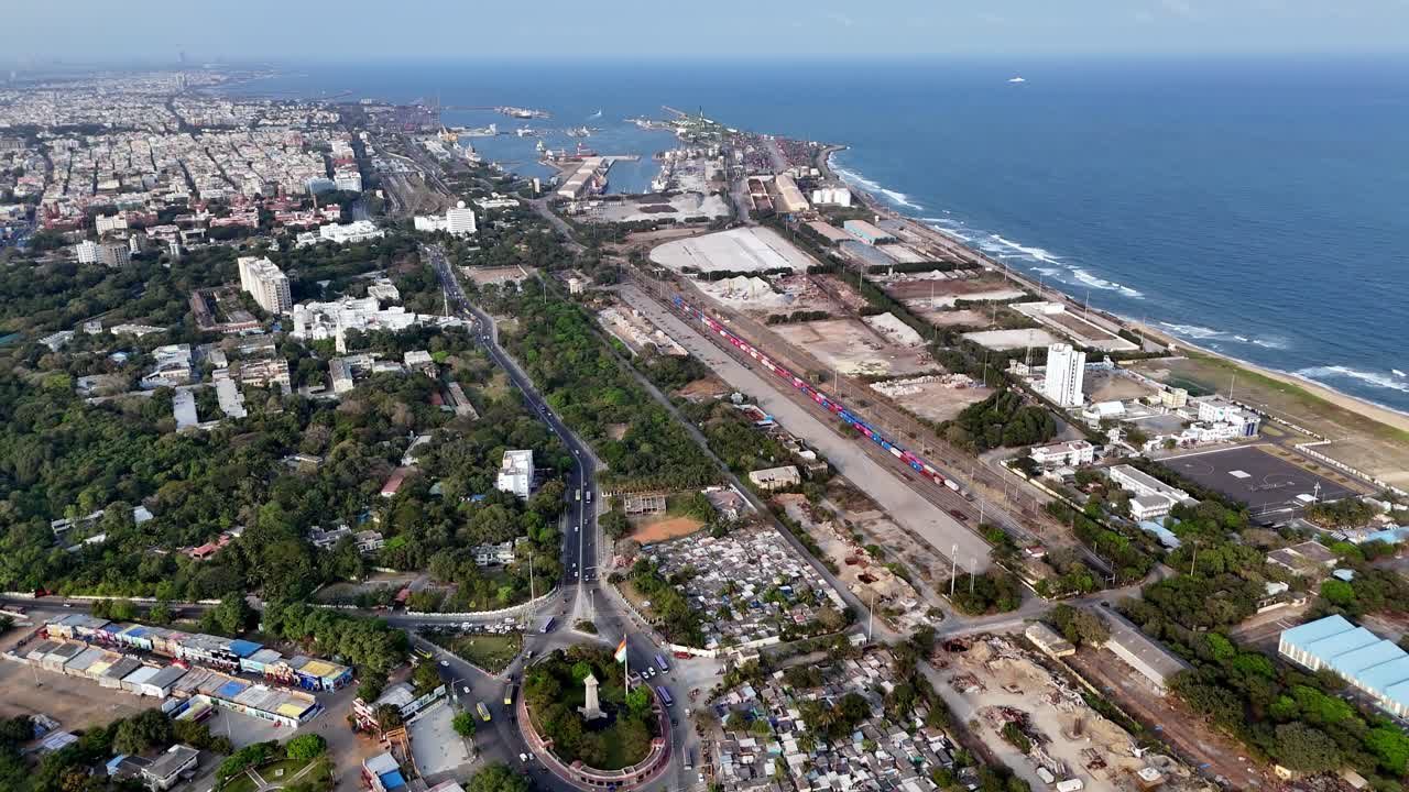 Vista panoramica aerea della costa settentrionale di Chennai, che mostra il Porto di Chennai, i piazzali container, le linee ferroviarie e il Golfo del Bengala. I quartieri urbani si fondono con l'infrastruttura industriale.