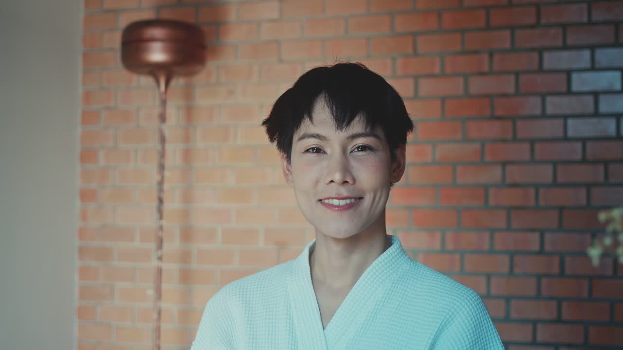 Woman in a bathrobe smiling in front of a brick wall