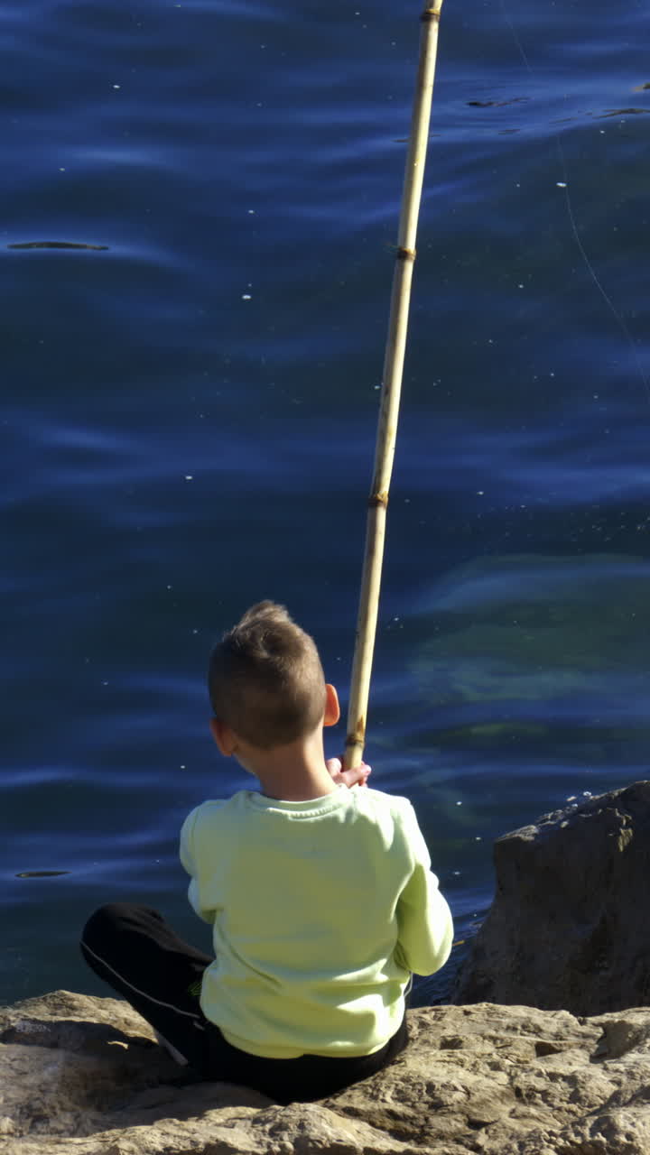 Anak kecil memancing di Laut Liguria pada siang hari. Vertikal