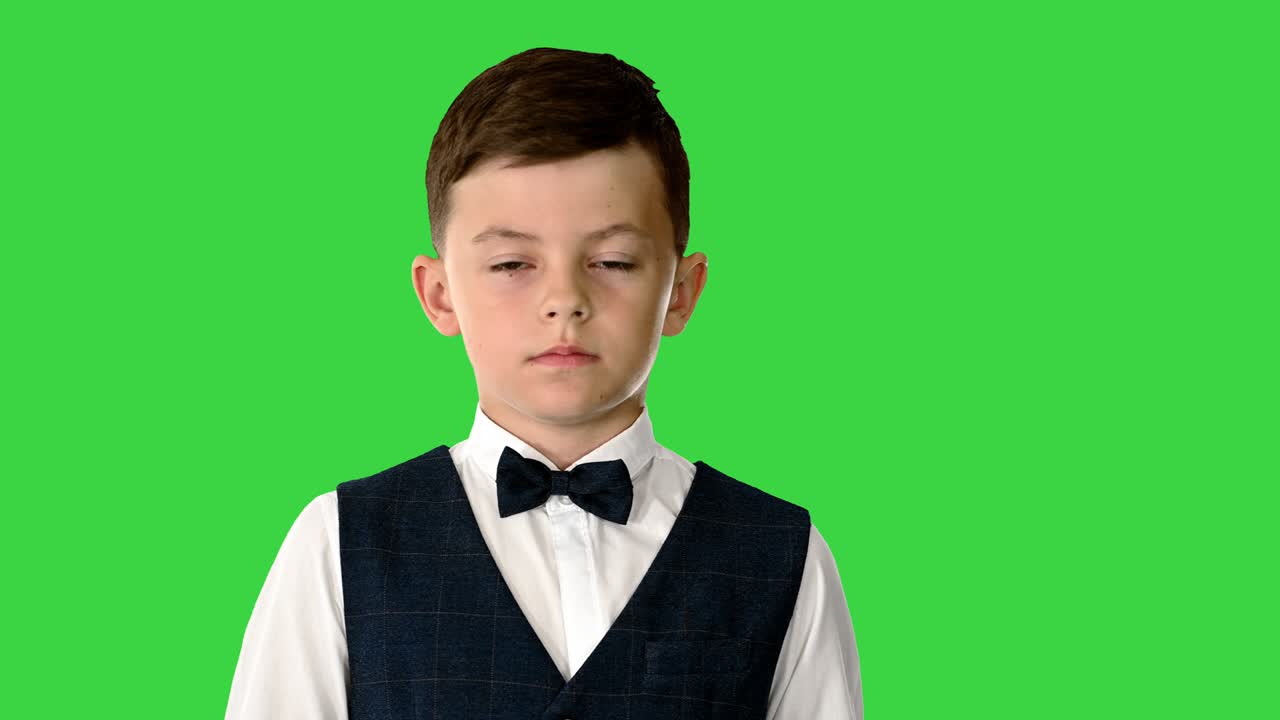 타이와 웨스트를 입은 작은 소년이 녹색 스크린에서 카메라와 이야기하고 있습니다.