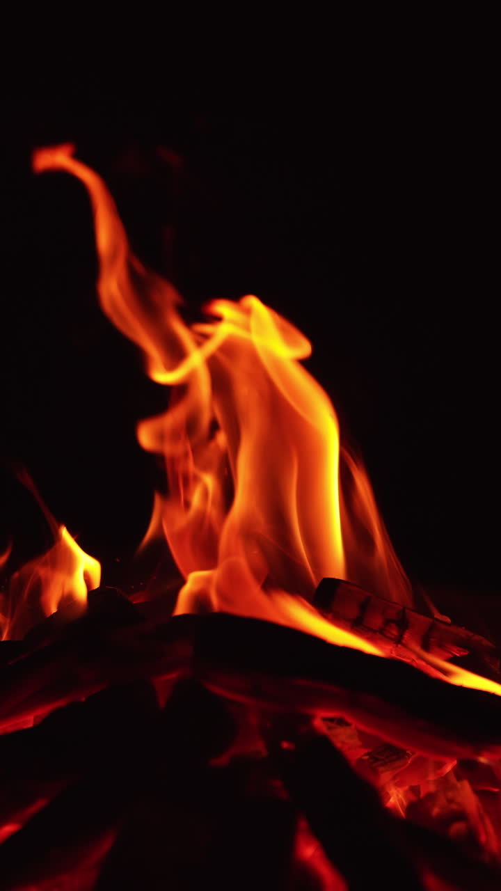 Una catasta di legna che brucia nella notte. Un accogliente falò che arde nell'oscurità. Video verticale