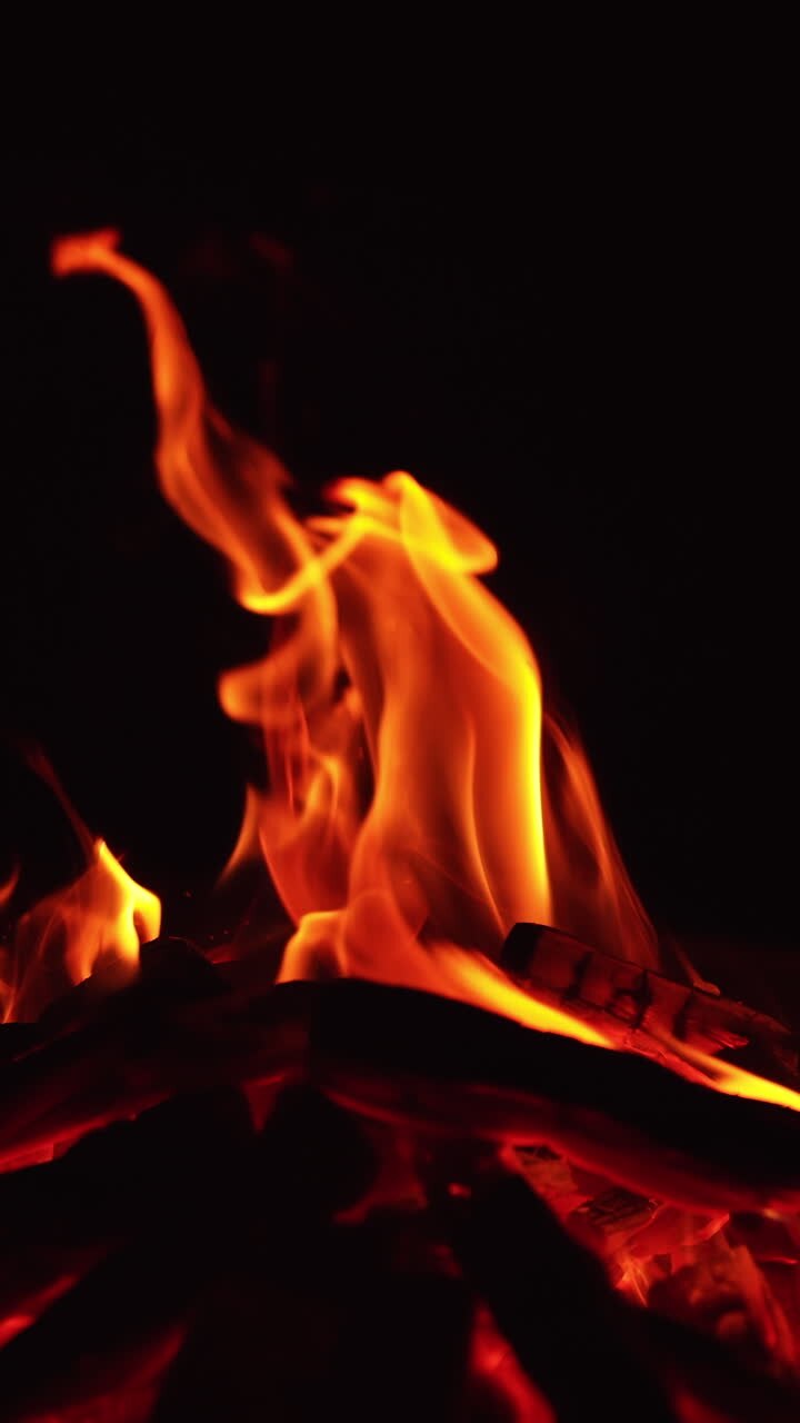 Una catasta di legna che brucia nella notte. Un accogliente falò che arde nell'oscurità. Video verticale