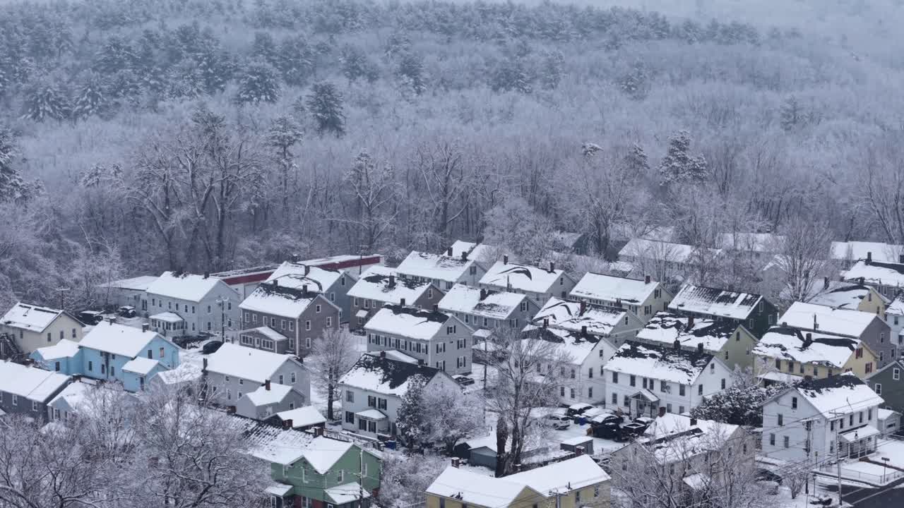 Suburbio de Nueva Inglaterra con nieve cayendo sobre los tejados de los pisos y casas adosadas al borde del bosque