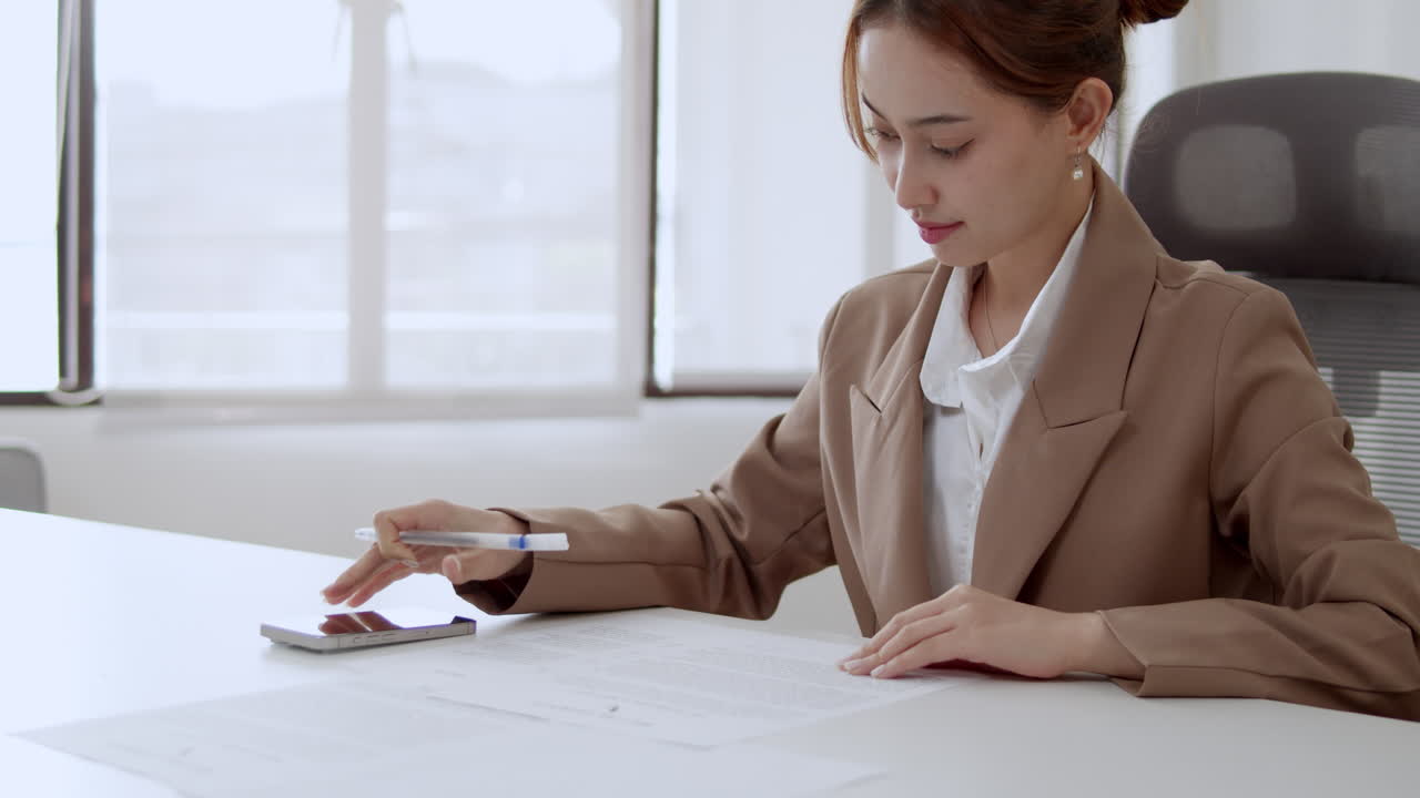 A female business owner reads important documents, signs them, and captures a photo with her phone to keep a record of the information for future reference.