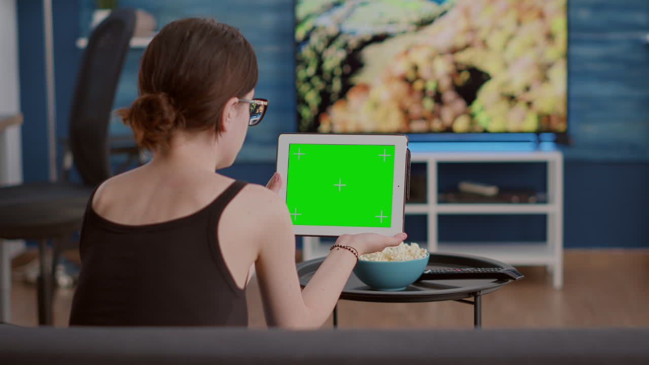 Back view of young woman holding digital tablet with green screen watching social media video content