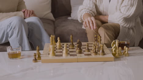 two senior women playing chess sitting on sofa at home 3