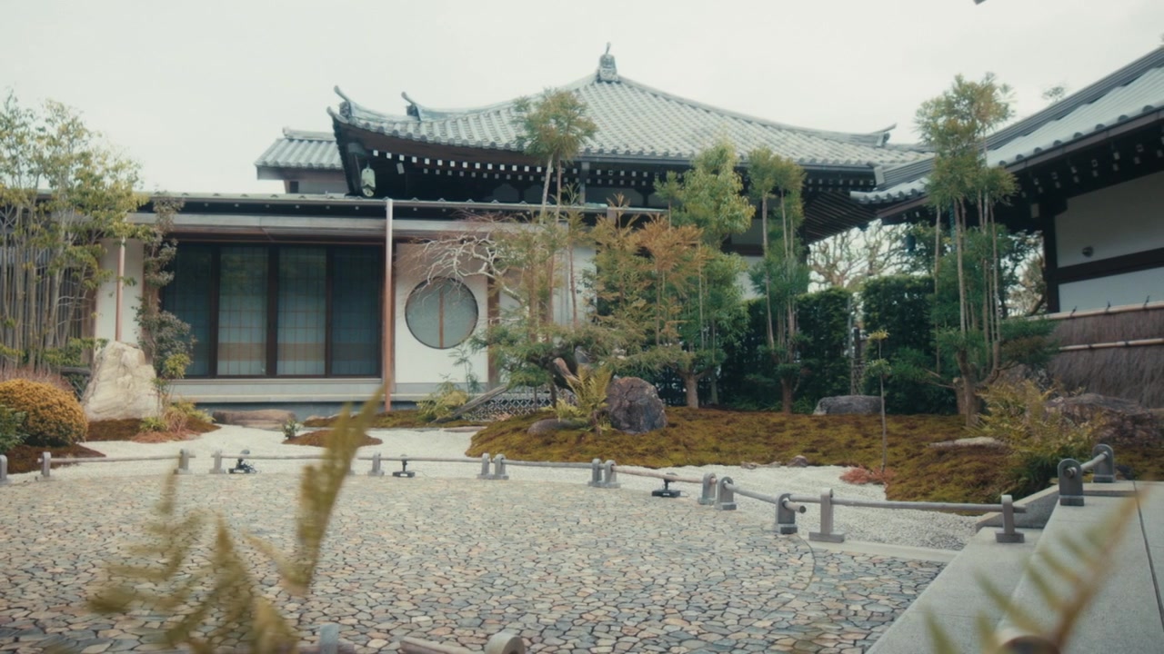 En fredfyldt udsigt over en traditionel japansk sten- og bambushave ved Hase-dera templet i Kamakura, med omhyggeligt placerede sten og revne grusstier ved siden af en trætempelbygning.