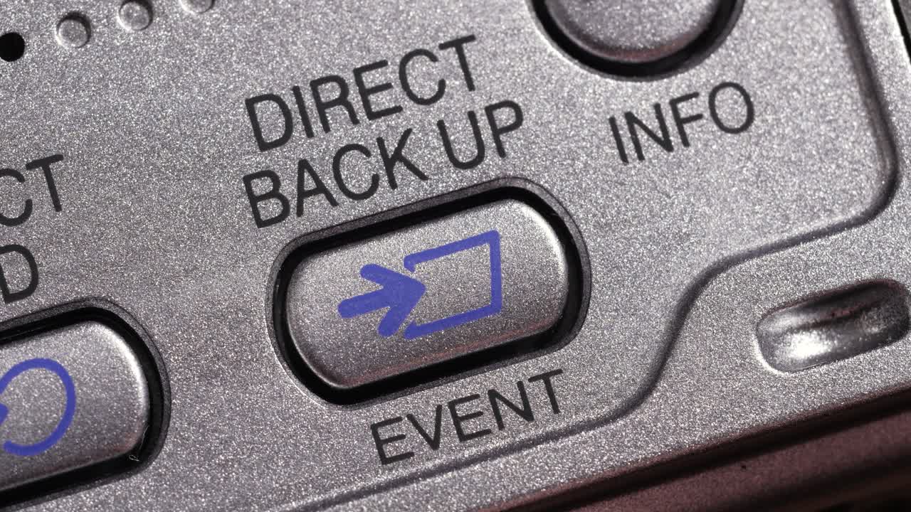 Angled macro close up of direct back up button pressed on metallic silver panel with blue icon