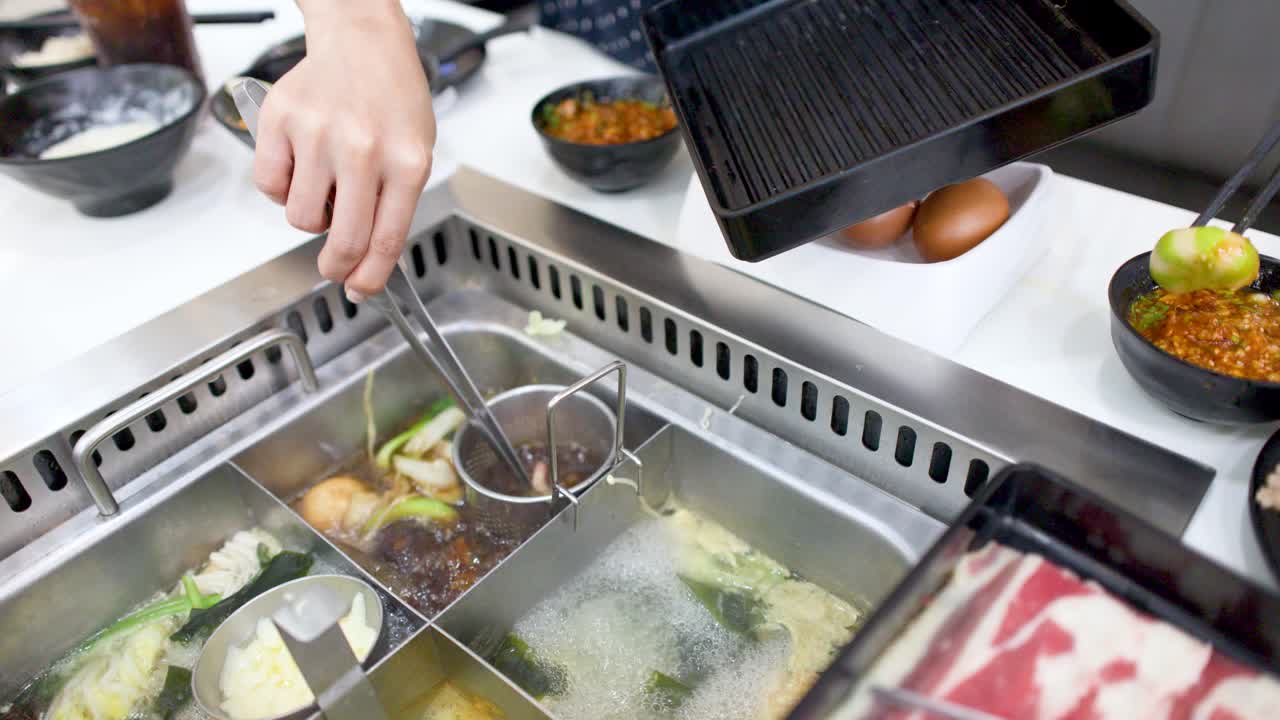沸騰した出汁の中で、トングを使って薄切り牛肉を調理する手のクローズアップショット。