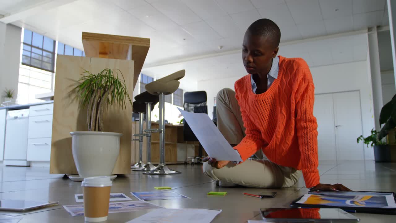 Low angle view of young black businesswoman working and sitting on floor of modern office 4k