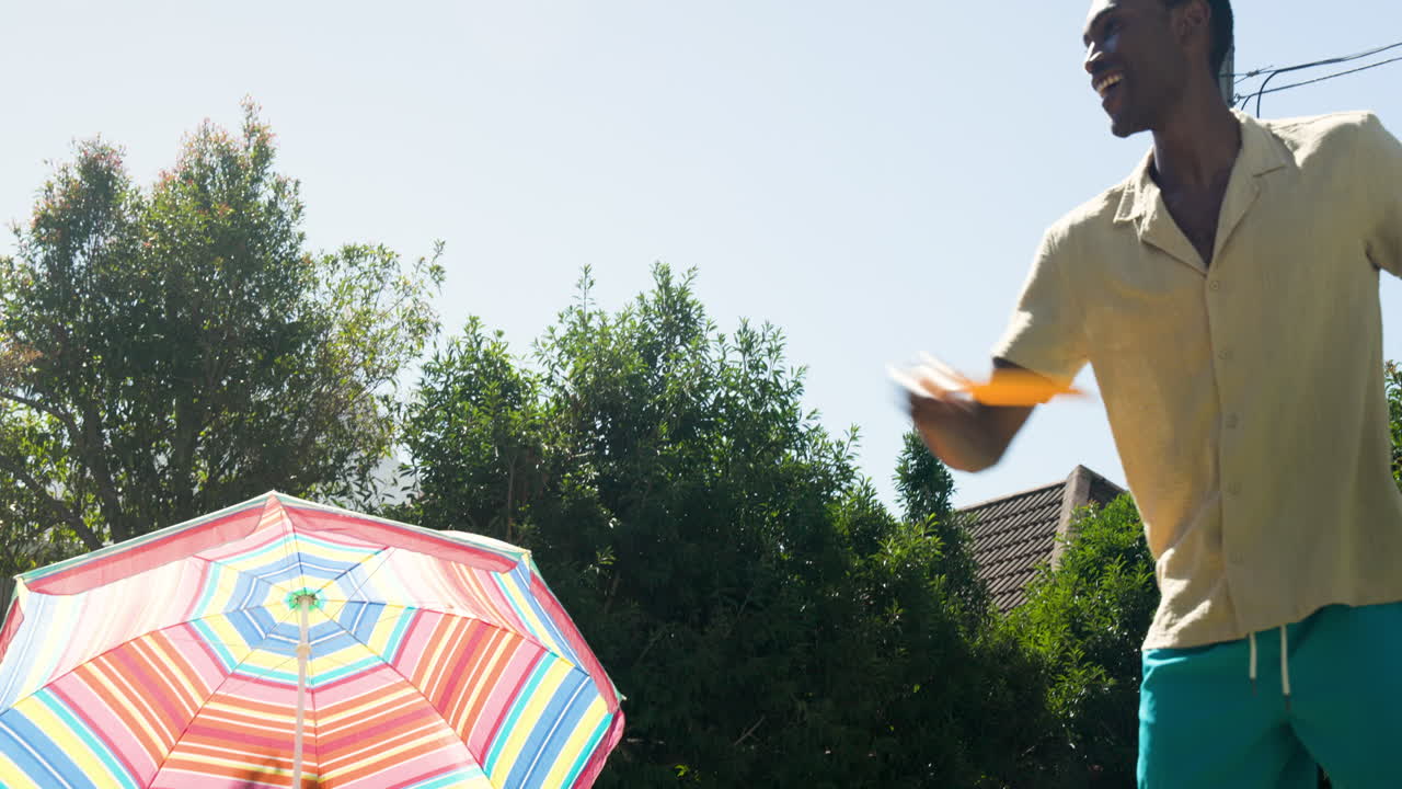 Man enjoying sunny day by pool with colorful umbrella and trees
