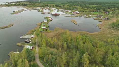 fly over autumn lake landscape with red cottages during cloudy day in finland