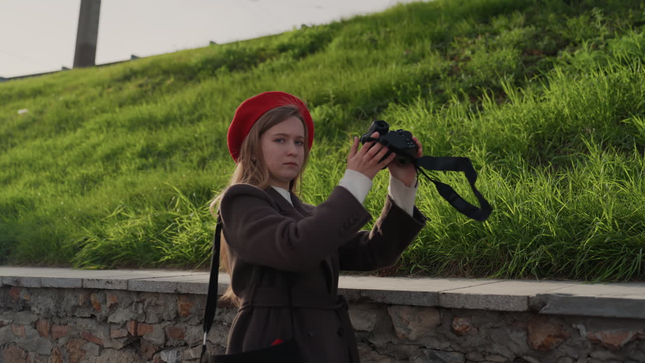 Entusiasta de câmera urbana. Fotógrafo revisa a lente enquanto se apoia em um muro de pedra na cidade. Artista de rua caucasiano inspeciona cuidadosamente sua câmera vintage em meio a um cenário urbano movimentado.