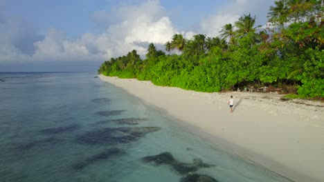 Static-aerial-view-of-man-walking-peacefully-through-tropical-beach-in-Maldives-at-sunrise