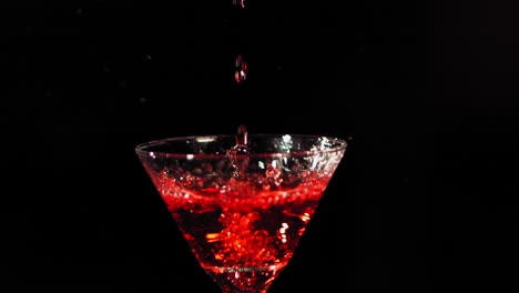 a red liquid is poured into a martini glass