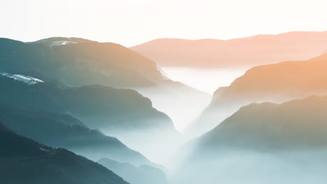 Timelapse-of-valley-with-fog-flowing-between-mountains-at-sunset