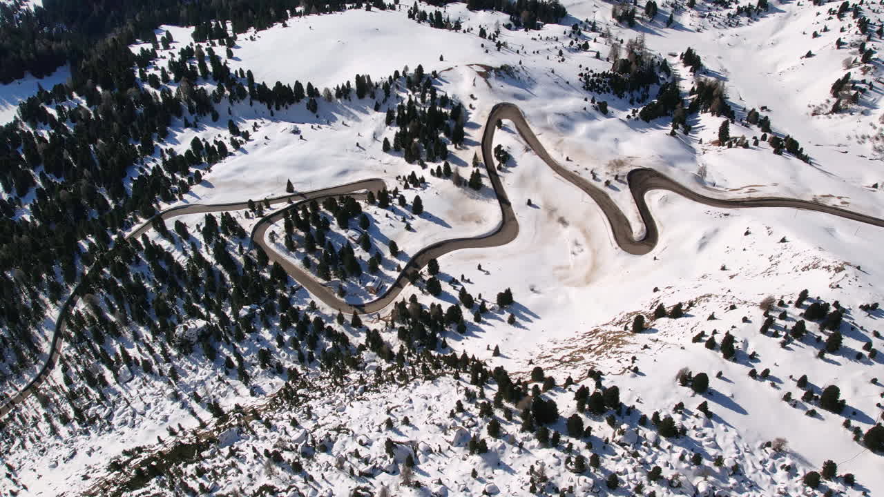 Aerial view of a winding mountain road through snow-covered terrain in the Dolomites.