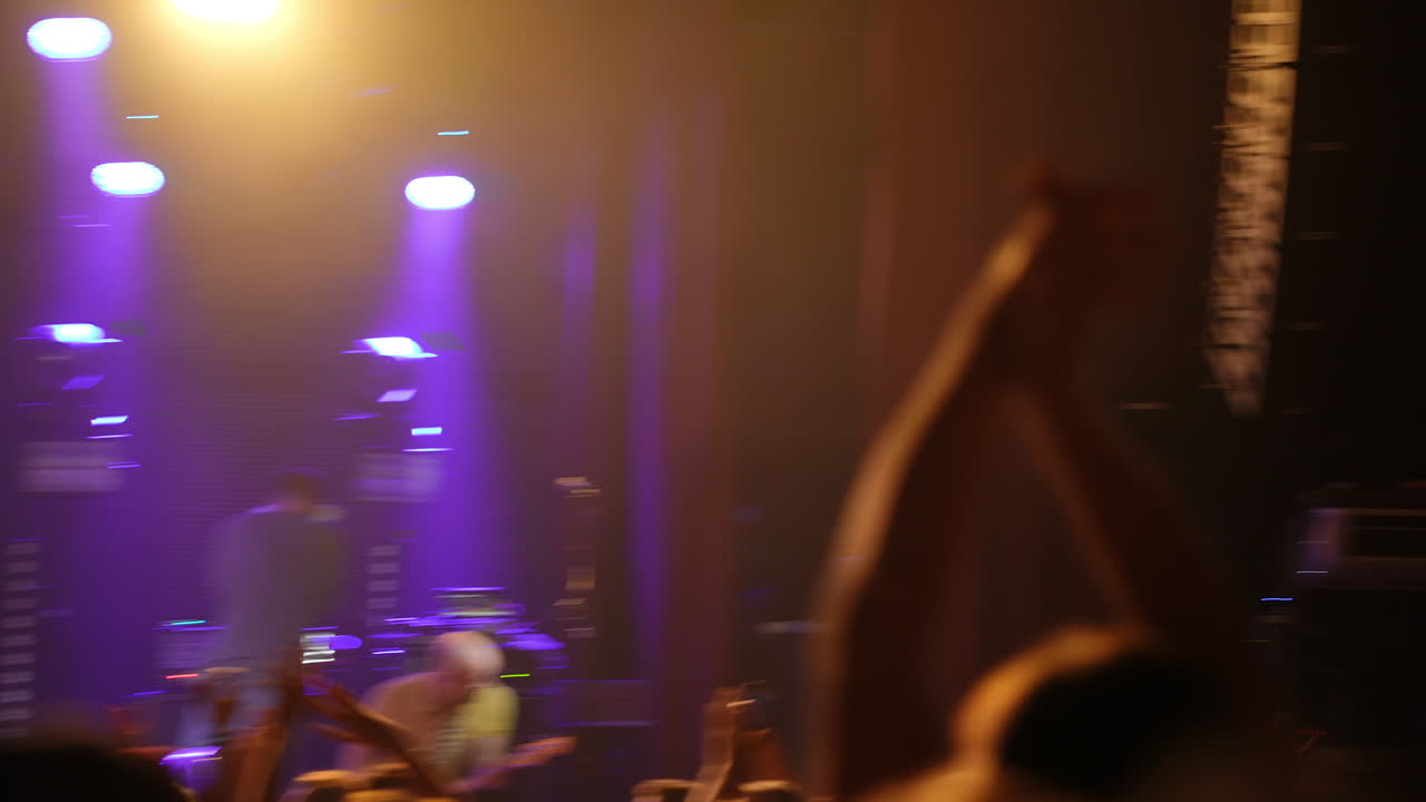 Pubblico a un concerto dal vivo con le mani alzate che si gode la performance, illuminato da luci di scena vibranti che creano un'atmosfera energica di celebrazione ed eccitazione