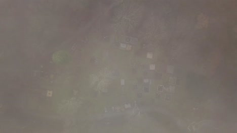 Aerial-top-down-descends-to-old-graveyard,-fading-from-white-fog