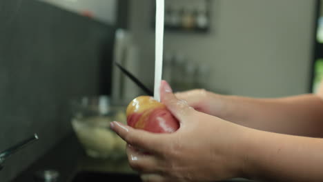 a woman peels potatoes under running water from a kitchen faucet.